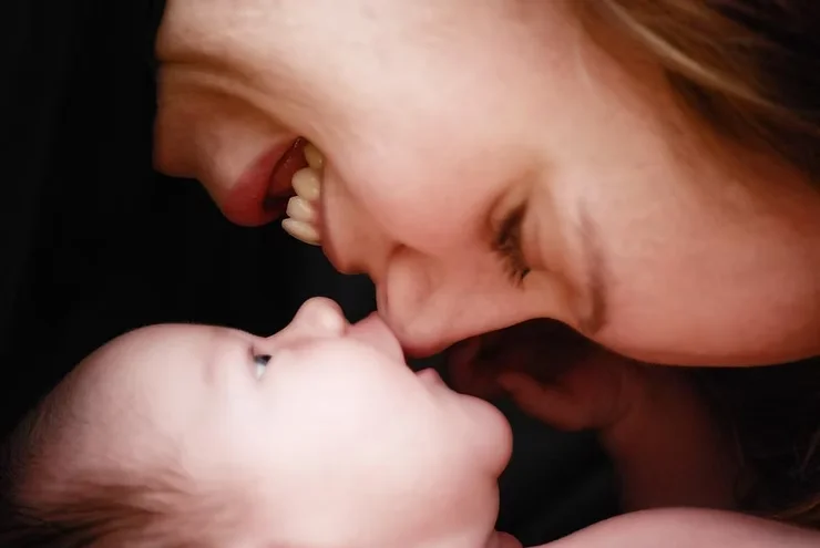 Primer plano de una madre sonriendo con su bebé recostado, rostro contra rostro, en un momento de conexión emocional.